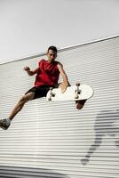 ung skateboarder hoppar upp med hans styrelse i främre av en metall bakgrund foto