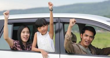 glad liten flicka med asiatisk familj som sitter i bilen för att njuta av roadtrip och sommarlov i husbil foto