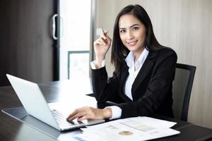 asiatiska affärskvinnor som håller en penna och analysdokument på kontorsbordet med bärbar dator och diagram över finansiella diagram som arbetar i bakgrunden foto