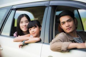 glad liten flicka med asiatisk familj som sitter i bilen för att njuta av roadtrip och sommarlov i husbil foto
