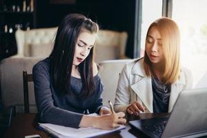 två asiatiska affärskvinnor som använder anteckningsboken och diskuterar det viktiga kontraktet på kontoret