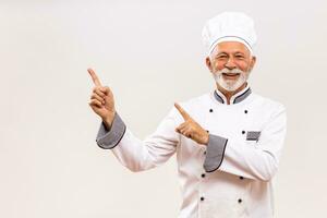 porträtt av senior kock pekande på grå bakgrund. foto