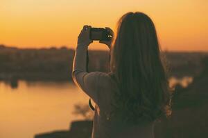 silhuett av en kvinna fotografering på de solnedgång. foto