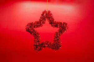 stjärna form prydnad hängande från topp på röd bakgrund. minimal jul Semester begrepp. foto