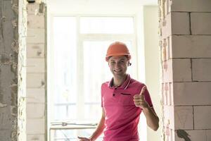 yrke, konstruktion och byggnad - Lycklig leende arbetstagare eller byggare i hjälm över rum med arbetssätt Utrustning på ny Hem eller lägenhet bakgrund foto