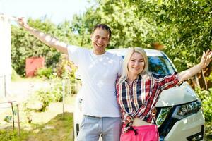 ny bil. ung vuxen glad man och kvinna stående med händer upp nära en ny bil, Lycklig foto