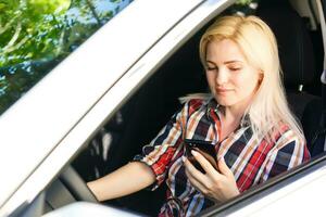 ung kvinna utseende på henne smartphone i en bil. foto