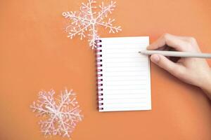 topp se av barn hand med innehav penna på vit papper tom anteckningsbok och skrivning önskar lista. foto