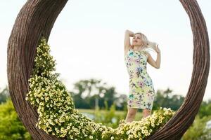 skön ung kvinna i trevlig klänning Framställ på färgrik vägg av blommor. mode Foto, trevlig hår, stor leende foto