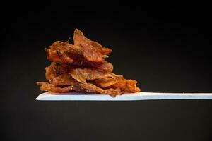 en näve av torkades kött marinerad med kryddor på en trä- sked, isolerat på en svart bakgrund. foto