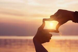 upptäckt inspiration och mål. en kvinnas händer skapa en ram och fokus med de solljus lysande ljust i de morgon. foto