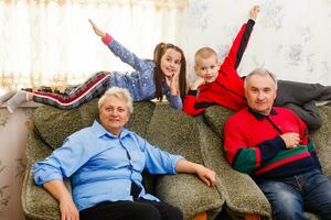 barnbarn Hoppar på soffa med deras farföräldrar i de levande rum foto