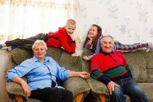 barnbarn Hoppar på soffa med deras farföräldrar i de levande rum foto