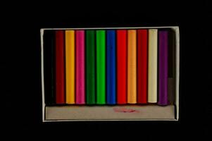 en låda av färgad pennor på en svart bakgrund foto