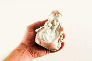 en hand innehav en porslin statyett av de jungfrulig och barn foto