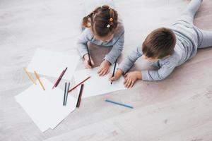 barn ligger på golvet i pyjamas och ritar med pennor. söt barnmålning av pennor