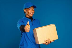 skön afrikansk kvinna kurir arbetstagare innehav en låda, gör en tummen upp gest foto