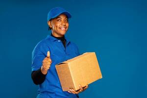 skön svart kvinna kurir arbetstagare innehav en låda, gör en tummen upp gest foto