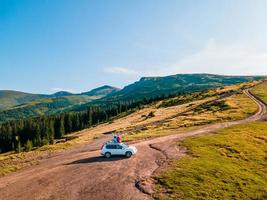 flygfoto över par som sitter på suv -biltaket och njuter av utsikten över bergen foto