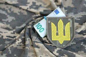 ukrainska armén symbol och knippa av euro räkningar på militär enhetlig. betalningar till soldater av de ukrainska armén från europeisk union, löner till de militär. krig Stöd foto