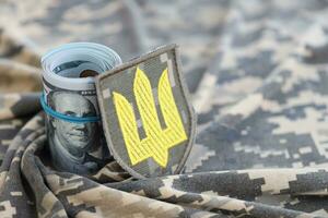 ukrainska armén symbol och knippa av dollar räkningar på militär enhetlig. betalningar till soldater av de ukrainska armén från förenad stater, löner till de militär. krig Stöd foto