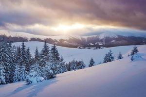 majestätisk solnedgång i den lilla byn på en snöig kulle under ukrainska. byar i bergen på vintern. vackert vinterlandskap. karpater, Ukraina, Europa foto