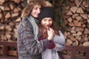 midja upp porträtt av sorglös ung man och kvinna som omfamnar och ler. de står i vinterskogen och tittar på kameran med lycka foto