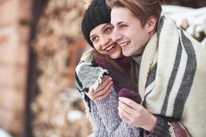 midja upp porträtt av sorglös ung man och kvinna som omfamnar och ler. de står i vinterskogen och tittar på kameran med lycka foto