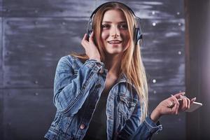 mode, kläder, människor koncept. närbild attraktiv sexig ung kvinna med jeansjacka. flicka poserar i studion lyssnar på musik i hörlurar