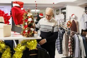 äldre kund verifierande objekt på ställ, ser till köpa kläder under jul säsong- försäljning. köpare sökande för handelsvaror på försäljning, framställning för Semester middag med familj, xmas handla. foto