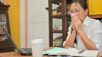 asiatisk kvinna använder en vävnad för att täcka hennes ansikte och nysa. hon arbetar hemma för att skydda mot corona-viruset eller covid-19. foto