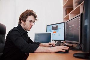manlig programmerare som arbetar på stationär dator med många bildskärmar på kontoret i programvaruutvecklingsföretag. webbdesign programmering och kodningsteknik