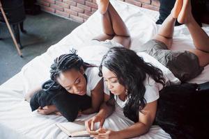 två vackra afrikanska flickor i sängkläder leende sitter på sängen hemma vaknade på morgonen på en solig dag.