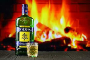 Kiev, ukraina - Maj 4, 2022 becherovka original- alkohol flaska på trä- tabell med röd öppen spis foto