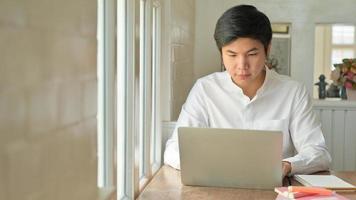 ung asiatisk man arbetar hemma med sin bärbara dator för att skydda mot corona-virus eller covid-19. foto