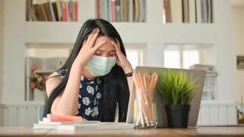 flickan bär en mask och rör vid huvudet hon arbetar hemma för att skydda mot covid-19-viruset.