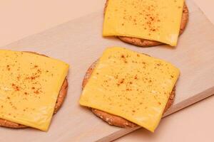 Krispig kracker smörgåsar med ost och paprika på trä- skärande styrelse och beige bakgrund foto