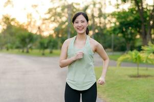 passa asiatisk ung kvinna joggning i parkera leende Lycklig löpning och njuter en friska utomhus- livsstil. kvinna joggare. kondition löpare flicka i offentlig parkera. friska livsstil och wellness varelse begrepp foto