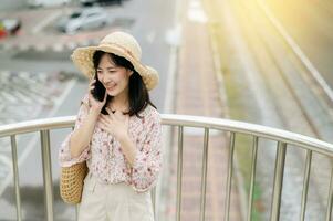 ung asiatisk kvinna resande med vävning korg använder sig av mobil telefon och stående på planskild med järnväg bakgrund. resa resa livsstil, värld resa explorer eller Asien sommar turism begrepp. foto
