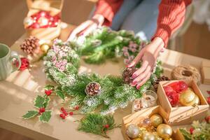 kvinna framställning mistel krans jul krans dekoration med hand tillverkad diy vinter- grönska blomsterhandlare händer framställning jul krans skön mistel. foto