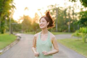 passa asiatisk ung kvinna joggning i parkera leende Lycklig löpning och njuter en friska utomhus- livsstil. kvinna joggare. kondition löpare flicka i offentlig parkera. friska livsstil och wellness varelse begrepp foto