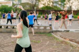 kvinna joggare. passa ung asiatisk kvinna med grön sportkläder aerobics dansa övning i parkera och njuter en friska utomhus. kondition löpare flicka i offentlig parkera. wellness varelse begrepp foto