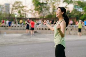 kvinna joggare. passa ung asiatisk kvinna med grön sportkläder aerobics dansa övning i parkera och njuter en friska utomhus. kondition löpare flicka i offentlig parkera. wellness varelse begrepp foto