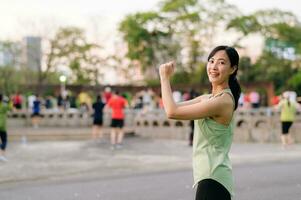 kvinna joggare. passa ung asiatisk kvinna med grön sportkläder aerobics dansa övning i parkera och njuter en friska utomhus. kondition löpare flicka i offentlig parkera. wellness varelse begrepp foto