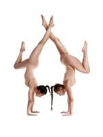 två flexibel flickor gymnaster i beige trikåer är utför övningar upside ner använder sig av Stöd och Framställ isolerat på vit bakgrund. närbild. foto