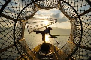 utsikt genom fiskkoppa av lokal fiskare som står på båt i sjön vid soluppgången foto