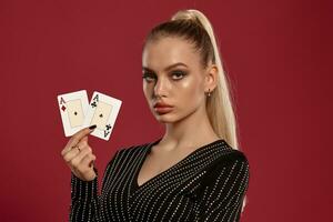 blond kvinna i svart klänning i strass. som visar två spelar kort, Framställ mot röd bakgrund. hasardspel underhållning, poker, kasino. närbild foto