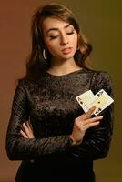 brunett flicka i svart sammet klänning och Smycken som visar två ess, Framställ mot färgrik studio bakgrund. spelande, poker, kasino. närbild. foto