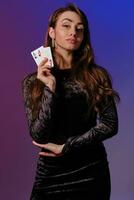 brunett kvinna i svart sammet klänning som visar två spelar kort, Framställ mot coloful bakgrund. hasardspel underhållning, poker, kasino. närbild. foto