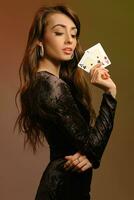 brunett kvinna i svart sammet klänning och Smycken som visar två ess, Framställ sidled på färgrik studio bakgrund. spelande, poker, kasino. närbild. foto